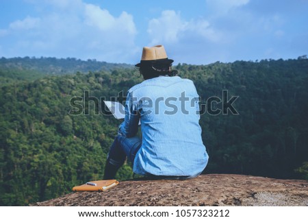 Asian man travel relax in the holiday. seats relax read books on rocky cliffs. On the Moutain summer. In Thailand