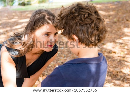 Portrait of mother who bends to talk to her son, outdoors.
Closeup of attractive woman facing young boy with brown curly hair. 
 Royalty-Free Stock Photo #1057352756
