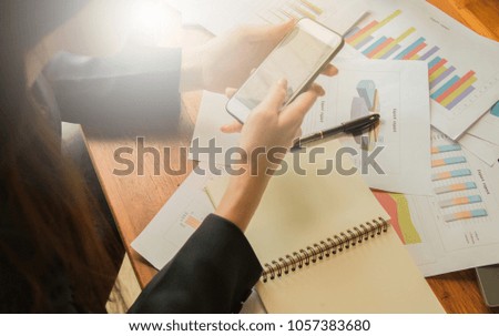 working woman use mobile to search data for create final report ,she have laptop,papers graph and paper note put on wooden table