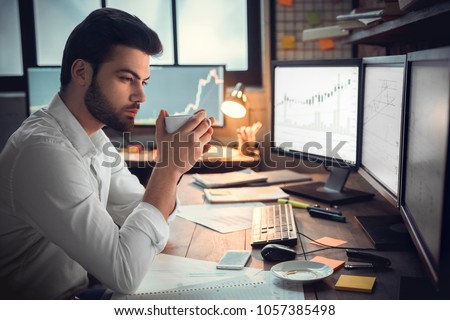 Thoughtful serious trader broker drinking coffee analyzing stock market graphs Royalty-Free Stock Photo #1057385498