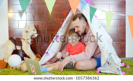 Happy little boy is watching cartoons with his father in the playroom