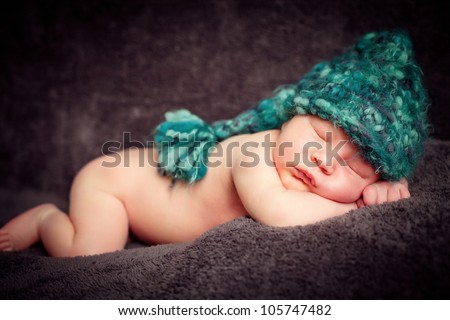 A newborn baby is wearing a blue hat and laying down sleeping on a soft braun background. Soft focus, shallow DoF.