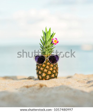 Summer lifestyle image of trendy girl-pineapple on the sand against turquoise sea. Wearing stylish sunglasses in the shape of heart and the flower in the tail. Tropical summer vacation concept. Sunny 
