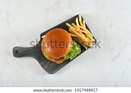 round hamburger with chicken cutlet and French fries on dark wooden Board - top view