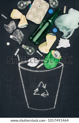 various types of trash falling into drawn trash can with recycle sign on chalkboard