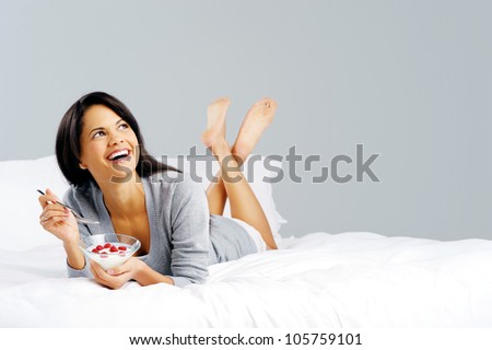 Portrait of a happy smiling latino hispanic woman eating a healthy breakfast of fruit and yoghurt in bed.