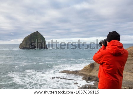 Adventurous man with a camera is standing taking pictures of the beautiful ocean during a vibrant winter morning. Taken in Cape Kiwanda, Pacific City, Oregon Coast, America.