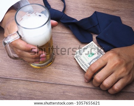 Men hand holding beer glass and banknotes on wooden table there necktie. Strain financial stress and work concept.