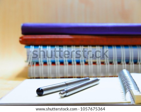 Closeup two silver pen on blank page of notebook with wooden background,Dual silver pen and many notebook on wooden