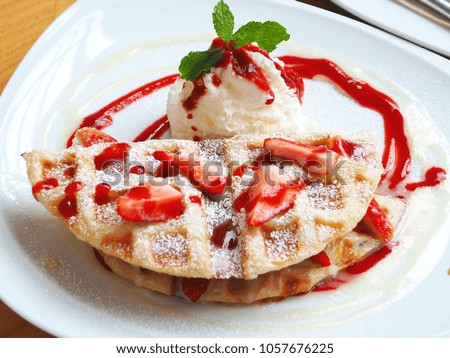 Closeup top view of roti milk waffle with slice strawberry, whipped cream and peppermint leaves on top in a white plate on wooden table, summer dessert