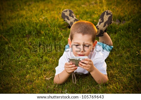 Preschooler boy lying on meadow and taking pic on their camera