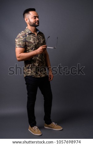 Studio shot of young bearded Indian man against gray background
