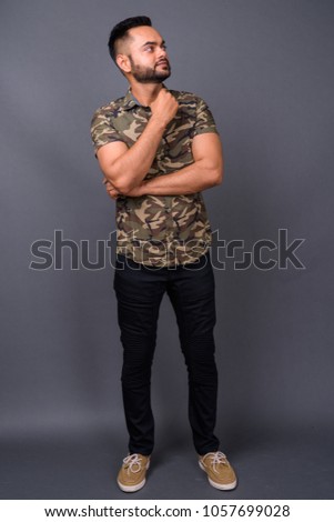 Studio shot of young bearded Indian man against gray background