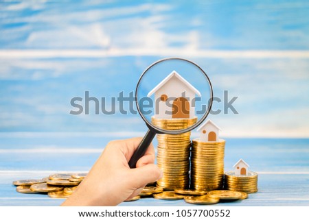 Woman hand hold a magnifier searching for new home and stack coin growing on the wood vintage blue background, Loan for real estate or saving money for buy a new house to family in the future concept.