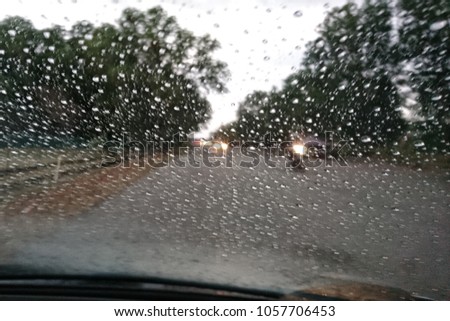 A very rare rainy day with car and people as seen through car windows with rain drops visible on the window. Blured background with rains drop on glass and cars on the road.- soft focus  