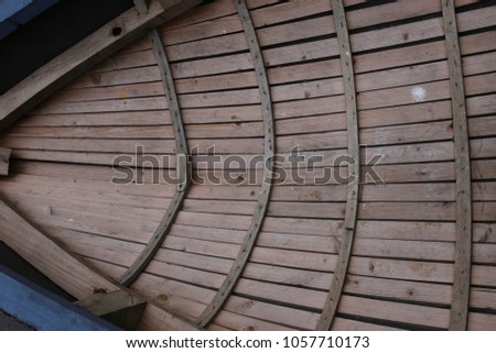 Close up outdoor view from above of part of a small wooden boat on the water. Particular design with wooden strips at the interior of the canoe. Curved shapes with clear brown lines. Abstract image.  