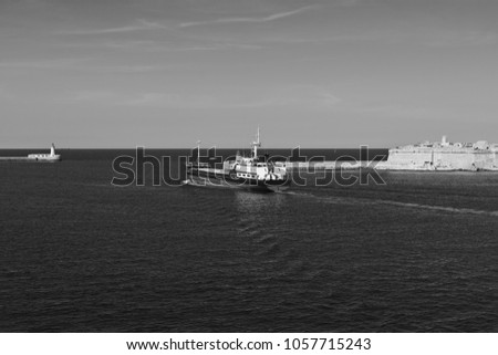 Cargo ship leaves the harbor of Valletta. Lighthouses indicate the entrance to the ports of Malta. Black and white picture