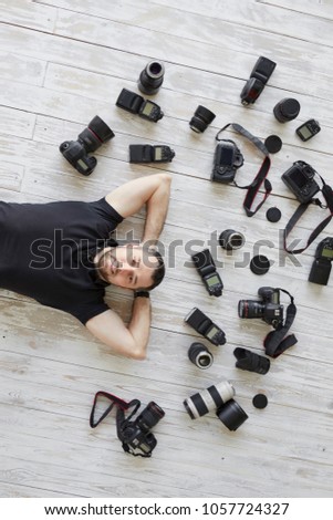 Many cameras and lenses lie on the floor around the photographer's man. Photographer