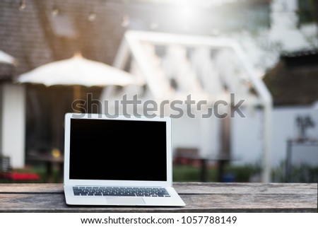 Blank screen laptop on wooden table blurred home background.