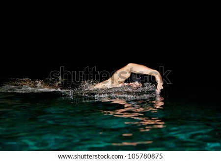 Man swimming in a swimming pool at night, training crawl style.