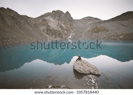 Small silhouette of traveler sitting on stone and staring at the lake.                              