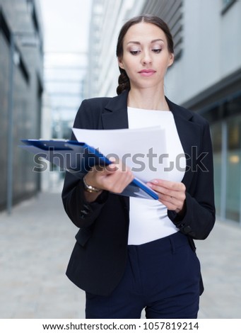 Female creative director is examining documents before signing outdoors.