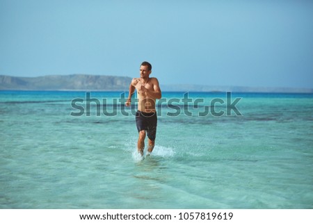 strong athletic man runs on the beach along the sea front. vacation and travel photography concept