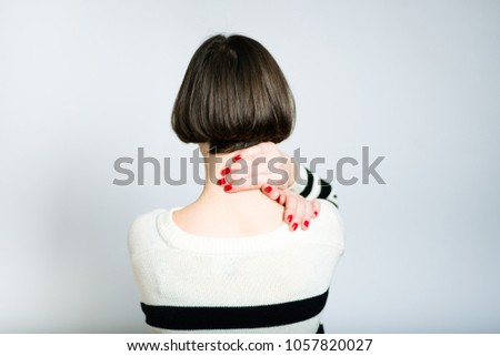 beautiful young woman has neck pain, short haircut, wears a sweater, isolated on gray background