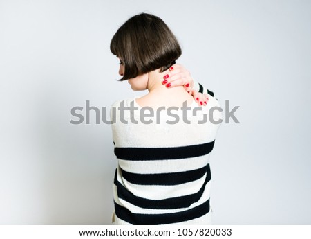 beautiful young woman has neck pain, short haircut, wears a sweater, isolated on gray background