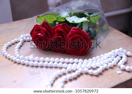 Pictured in the photo three beautiful red roses and pearl beads.