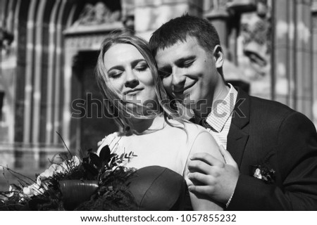 Black and white photo. Wedding day. Photoshoot after the wedding. Bridal bouquet. A blue-green dress. The couple is hugging. Against the backdrop of an ancient church.