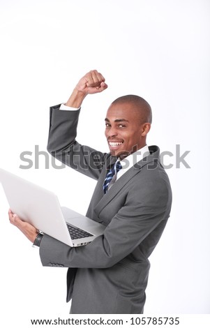 A happy attractive African American businessman wearing a corporate grey suit and blue tie holding a laptop computer, raising his fist up and punching the air in a triumphant move in a successful deal