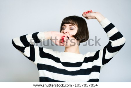 portrait of a beautiful young woman yawns, short haircut, wears a sweater, isolated on a gray background