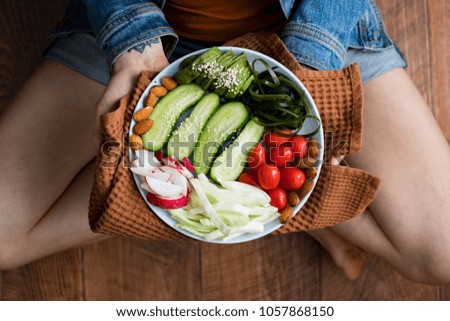 Woman hands holds Buddha Bowl with fresh vegetables. Cucumbers, tomatoes, radish, cabbage, avocado, almonds. Top view. Organic natural products. Raw, vegan, vegetarian healthy food