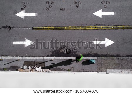Passenger with the bag stands on the street on which are arrow signs for direction, shot is from above, no recognizable person