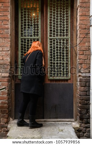 curious red-haired girl peeks into the house through the window of an old unusual door
