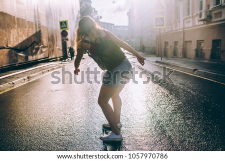 A stylish woman drives quickly down the street in a longboard, a rear view. Female skater moves on skateboard down street at sunset