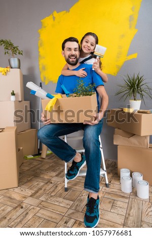 Little daughter with paintbrush hugs father, who keeps box of tools and things. Family does house repairs together. Moving to new apartment.