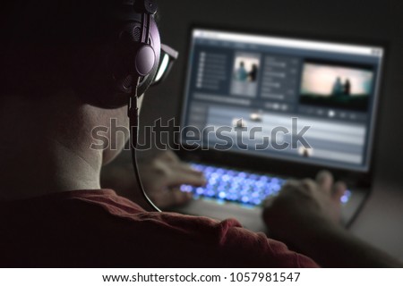 Video editing with laptop. Professional editor adding special effects or color grading footage. Back view of young man using computer software and wearing headphones.