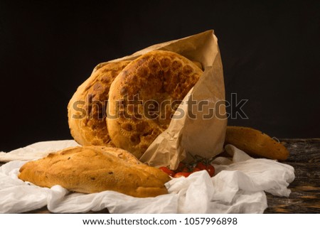 Conceptual still life art photography of a different kinds of bread wrapped in paper bag and cherry tomato branch on an ancient wooden table. Copy space. Advertising, cooking, bakery and commercial.