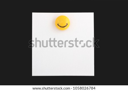 Note paper white with a cheerful yellow magnetic clip with a smile on a black background.