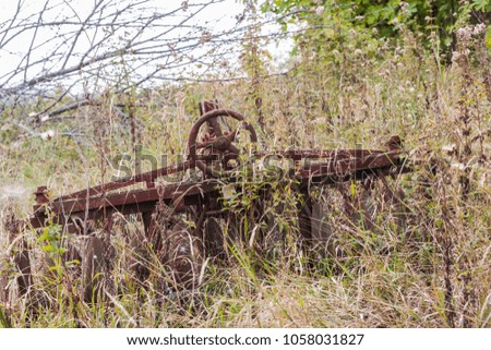 Agricultural machine abandoned in an overgrown field.