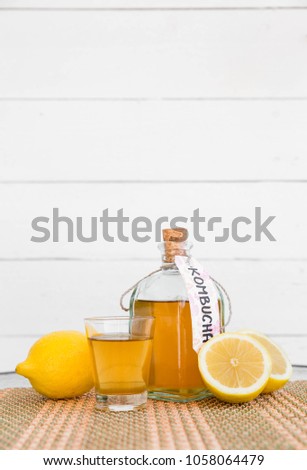 Fermented raw kombucha tea in a glass bottle and a glass, with label written kombucha on it, white wooden background. Space for text.