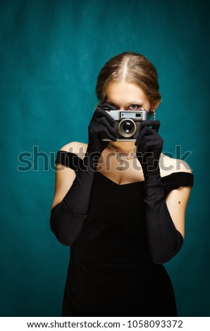 The girl in a black evening dress with a camera in her hands. The picture was taken in the studio, on a blue-turquoise background