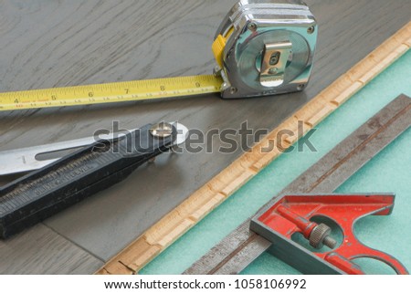 Engineered wooden flooring installation, showing a combination square, adjustable sliding bevel and tape measure. on cushion underlay. Royalty-Free Stock Photo #1058106992