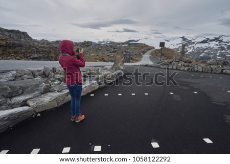 The girl takes pictures of the mountains in the parking lot on top of Dalsnibba Mountain.