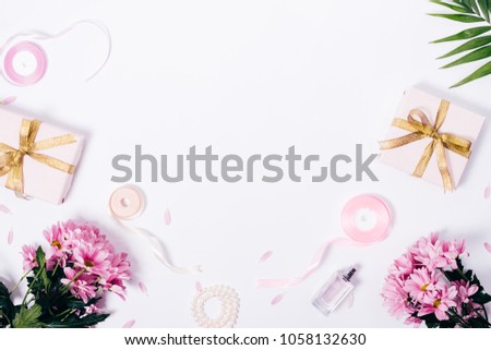 Feminine top view frame with copy space: lush pink flowers, perfume, pearls, gifts, golden ribbons and petals on white background. Festive composition expression of spring image with blank center.