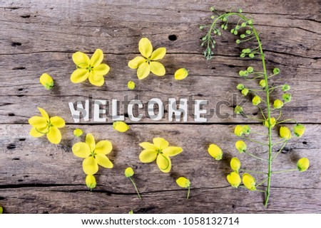 Word "welcome" with spring yellow flower on wooden background.