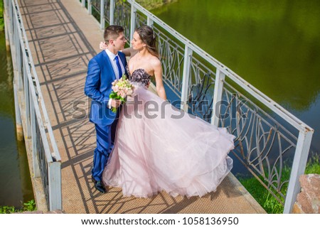 Groom and bride in pink dress walking together on bridge in park