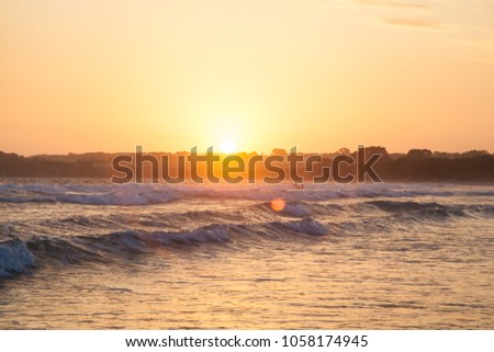 Sunset over beach in Victoria Australia in Inverloch with small waves and people in the background and coastline with slight lens flare.